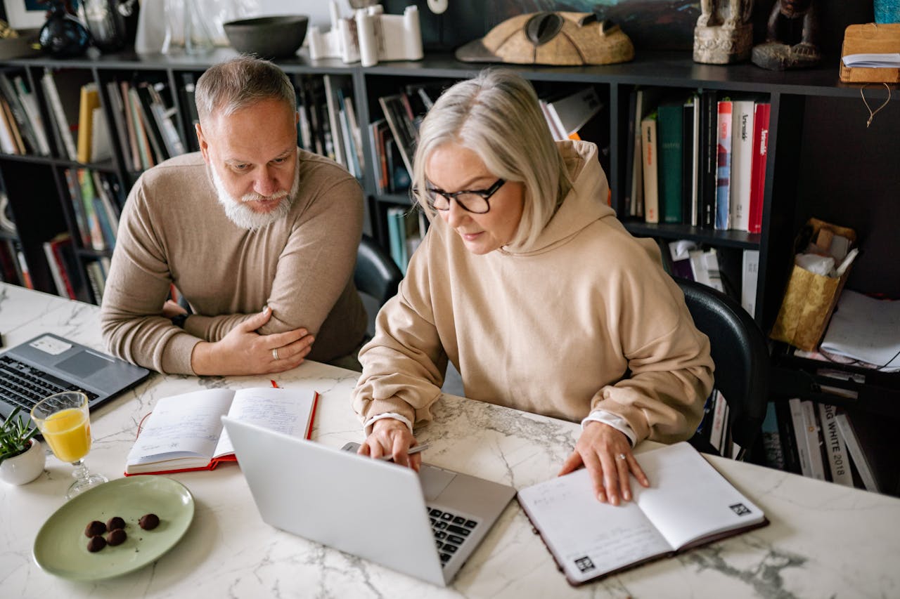 Elderly couple collaborating on laptops in a cozy home office setting.